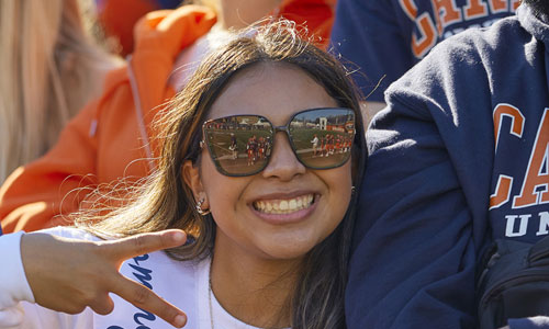 Smiling carroll student dressed in pio gear and giving peace sign with hand
