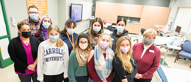 a group of students wearing face masks in a nursing class room.