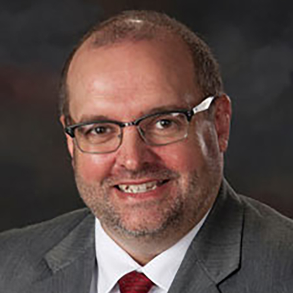 Professional man with a friendly smile wearing glasses, a dark suit, and a red tie.