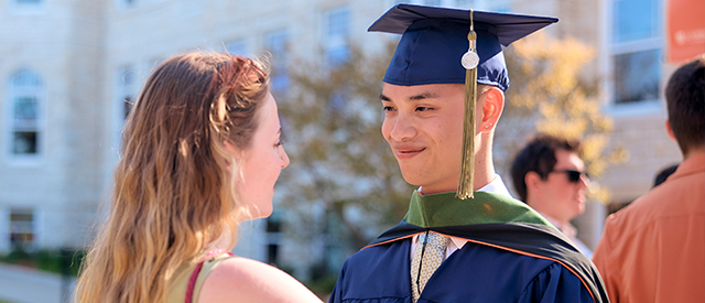 Women helping student put on cap and gown.