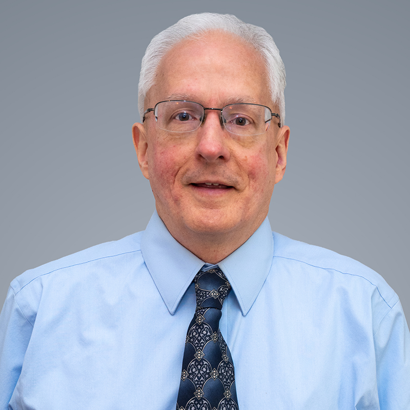Man in blue collared shirt with a tie smiling.