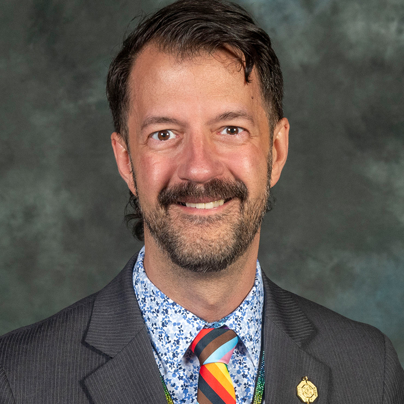Man in a grey suit with a rainbow tie. 