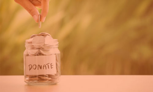 a hand putting money into a jar with the word donate written on it.