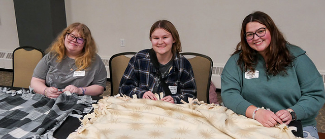 3 women making a tie blanket.