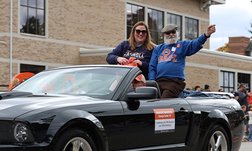 Man and Women riding in a convertible in parade.