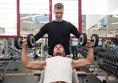 Man lifting weights in gym with trainer