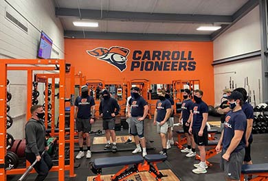 students learning from a coach in weight room