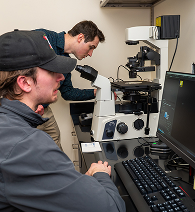 Professor Ben Hall helps student with microscope and computer