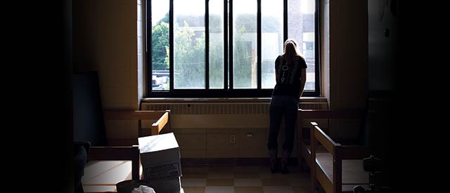 student looking out window in dorm room