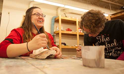a female student laughing while working on a sculpture