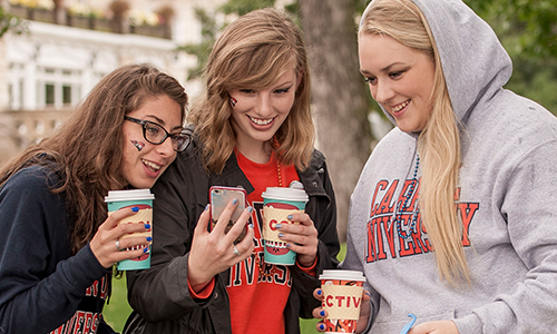 3 female students looking at phone with coffee 