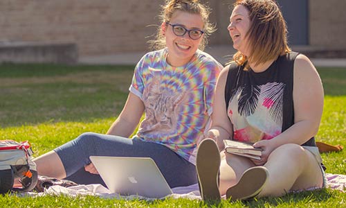 Two students sharing a laugh on Main Lawn while studying