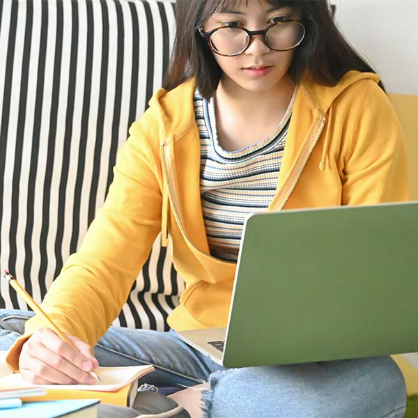 focused female student taking notes while looking at her laptop