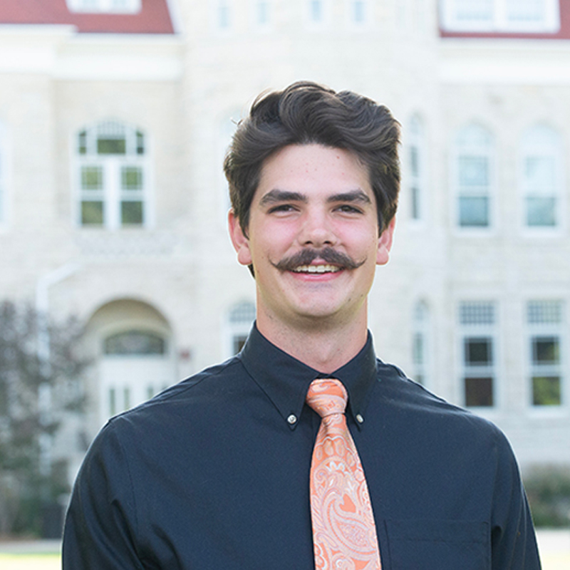 A man on a college campus wearing a black shirt with a orange tie.