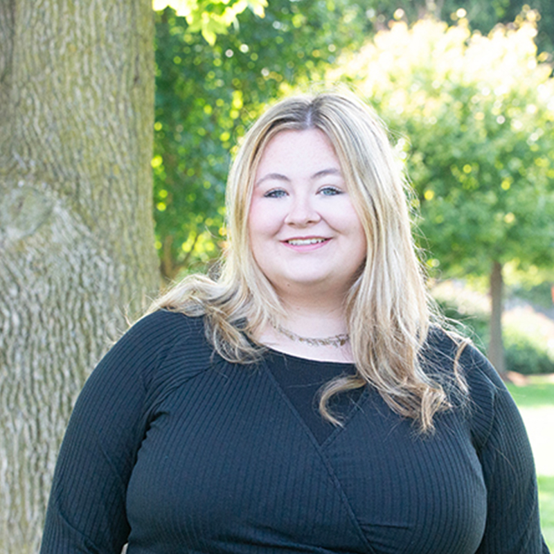 Women with blonde hair and a black shirt in front of a tree.