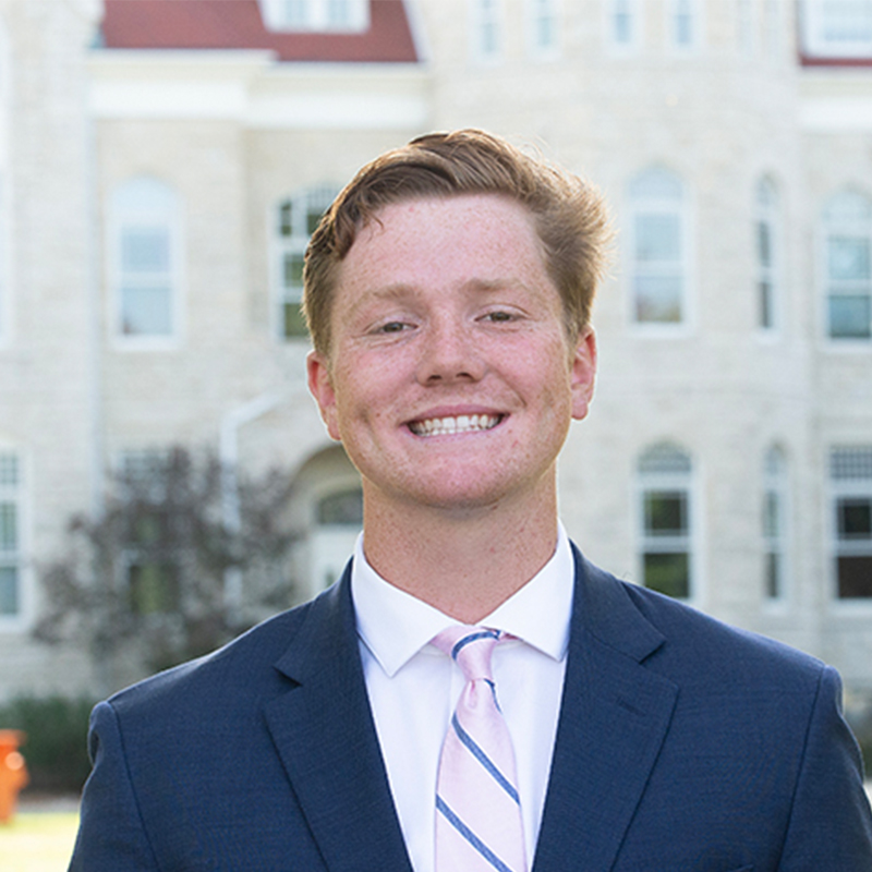Man on a college campus in a suit.