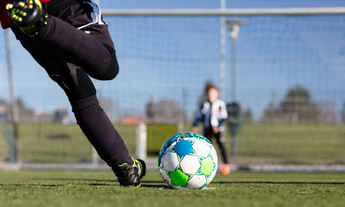a foot kicking a soccer ball toward goal
