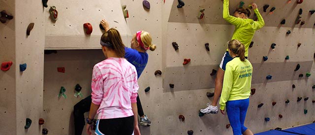 four girls climbing a rock wall inside Ganfield Gymnasium