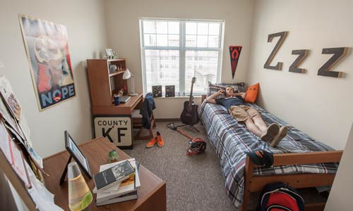 Photo of student talking on phone on bed in dorm room