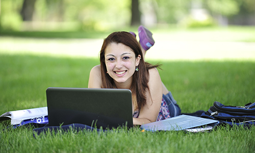 Smiling student with laptop on main lawn.
